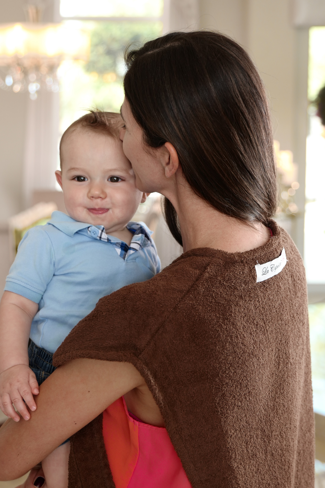 Woman wearing the chocolate La Capelette while holding a smiling baby.